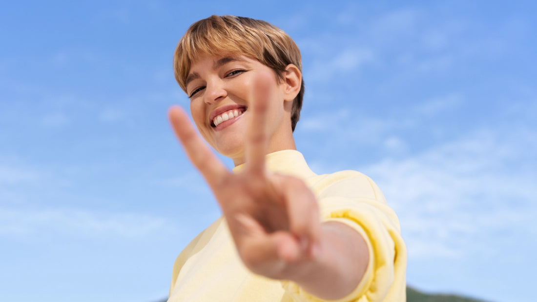 Woman making a victory sign with her hand against a blue sky.