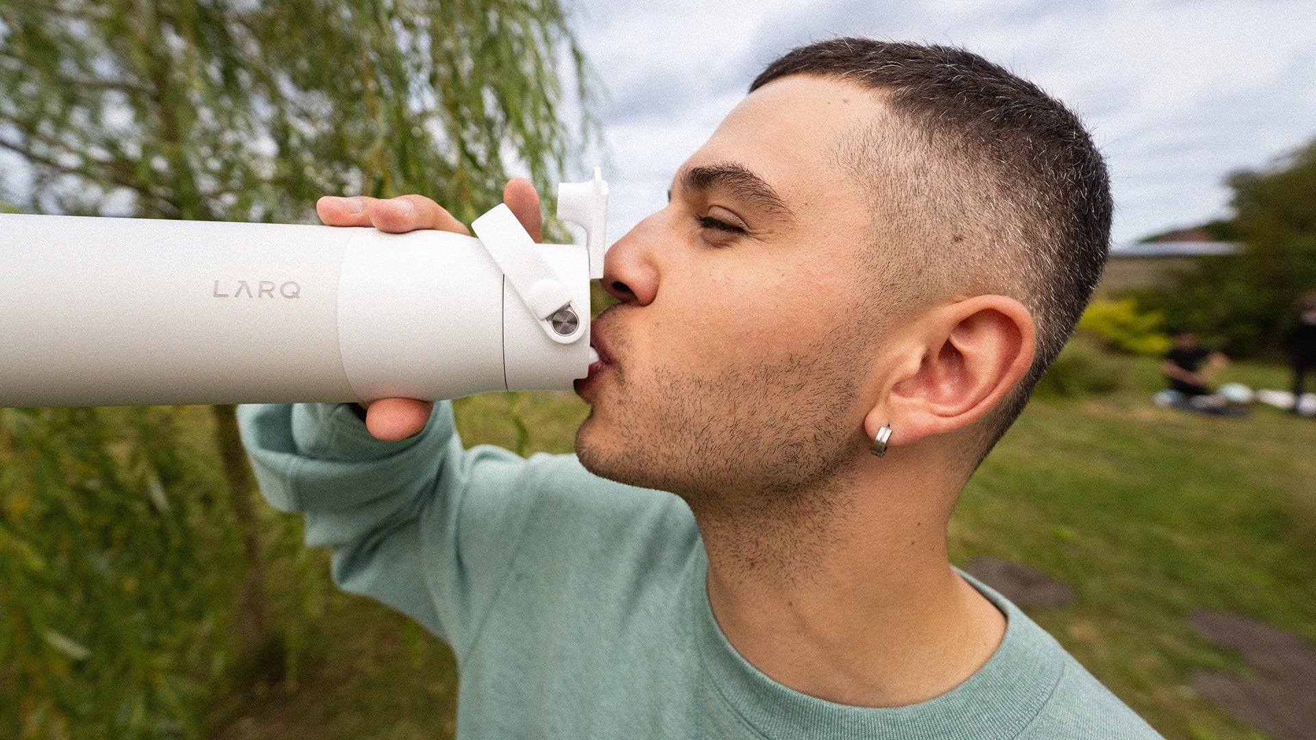 A man outdoors drinking from a BRITA LARQ Essential in white wearing a sage green sweatshirt.