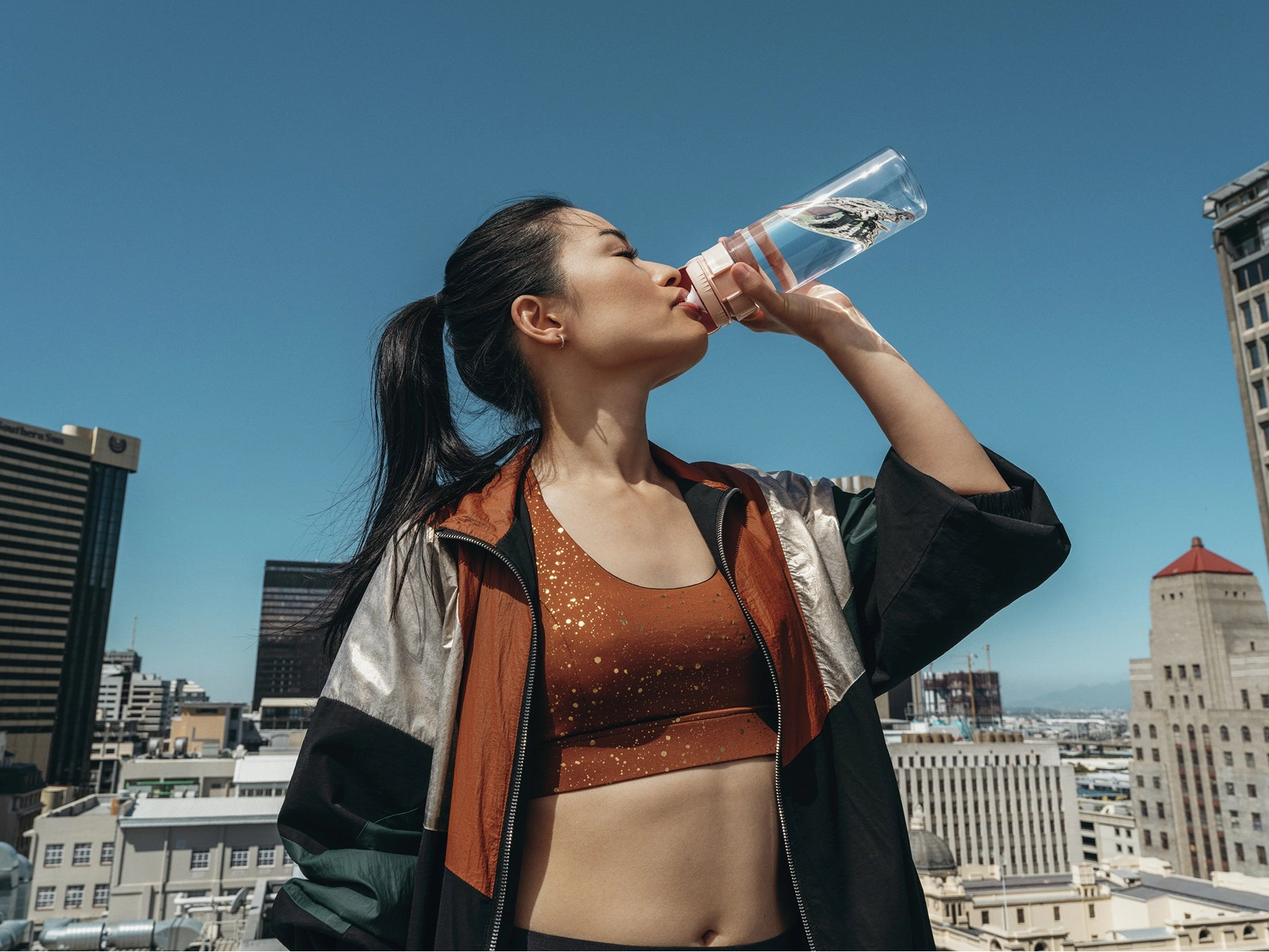 Woman drinking water with BRITA water filter bottle Model Vital on a rooftop with cityscape in the background