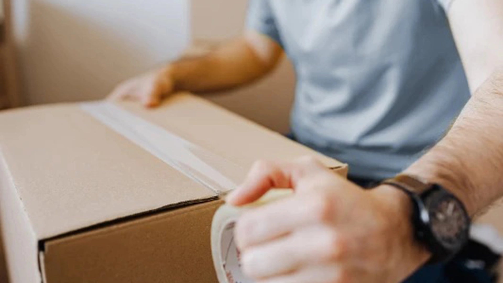 Person taping a cardboard box shut with focus on hands and box.