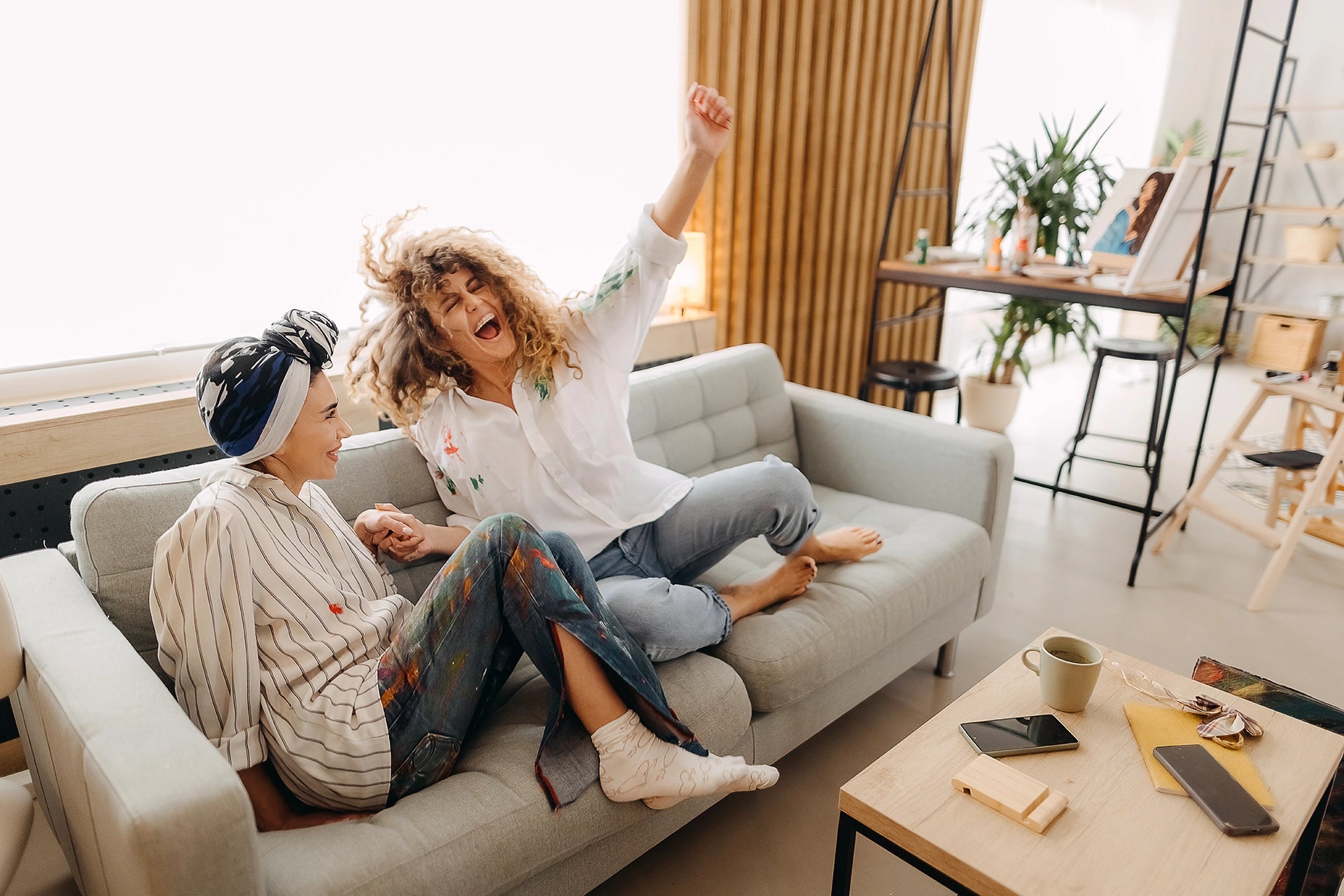 Two women are sitting on the sofa, laughing together.