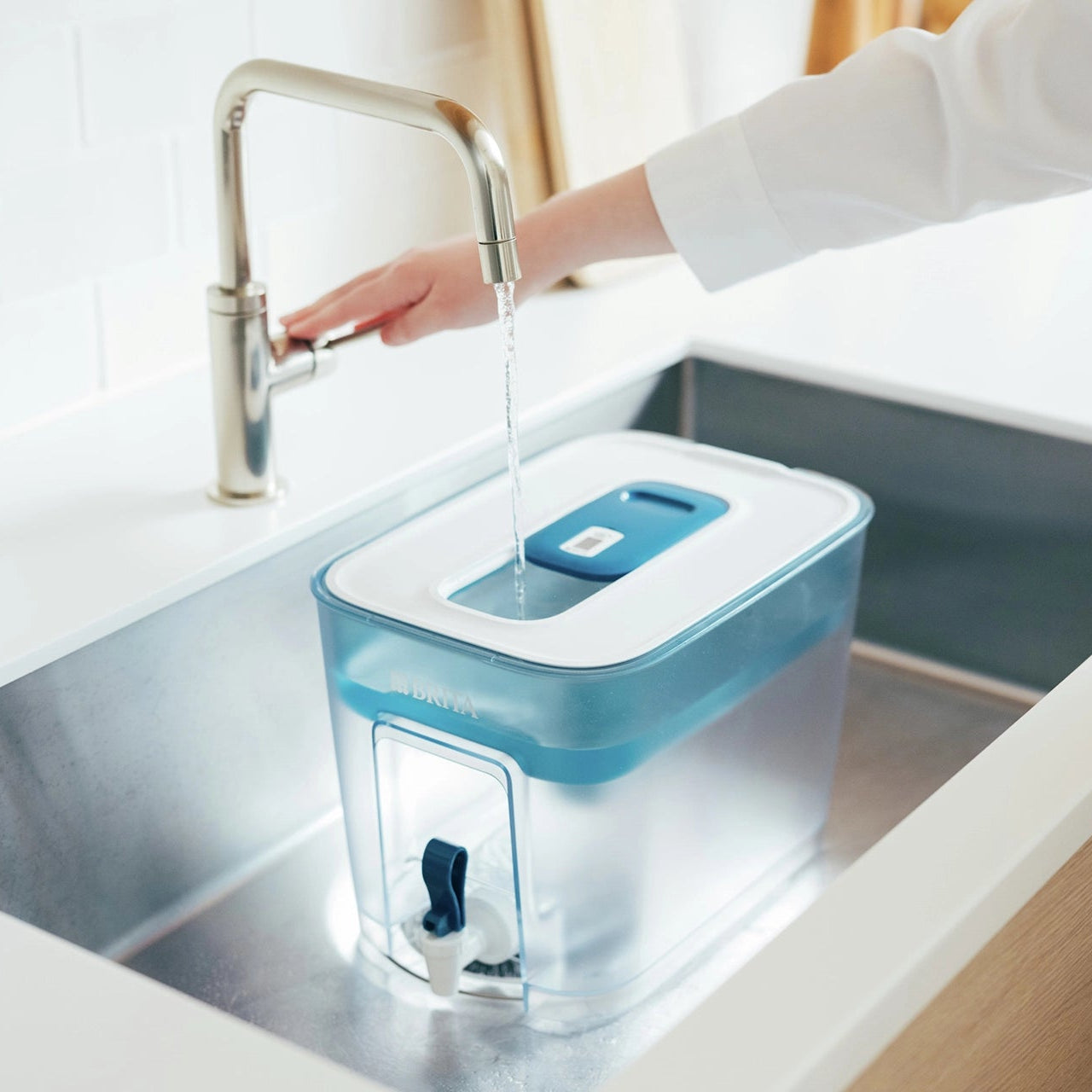 BRITA Flow agua filtro Un recipiente que se está llenando de agua en el fregadero de la cocina, bajo un grifo abierto.