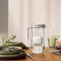 BRITA glass jug in grey on a wooden table with wine glasses and plates in the background