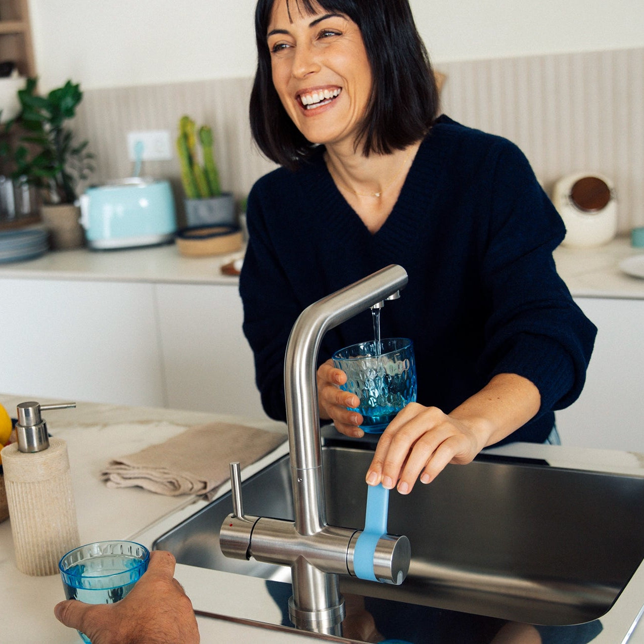 Una mujer vertiendo agua del filtro BRITA de tres salidas filtro se sirve un vaso en la cocina, con un hombre a su lado.
