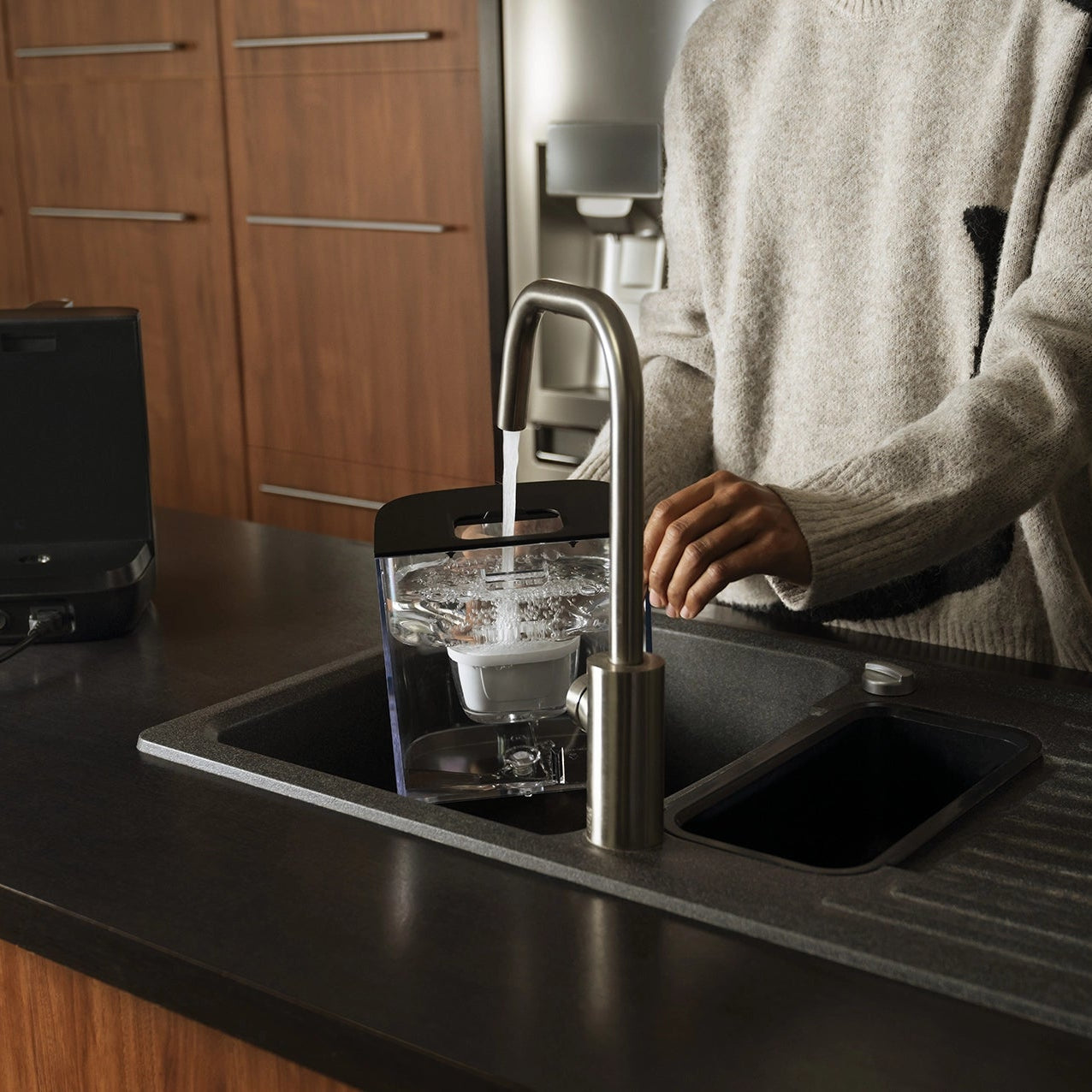 Person filling a BRITA YOURCE Mini water dispenser with tap water at a kitchen sink.