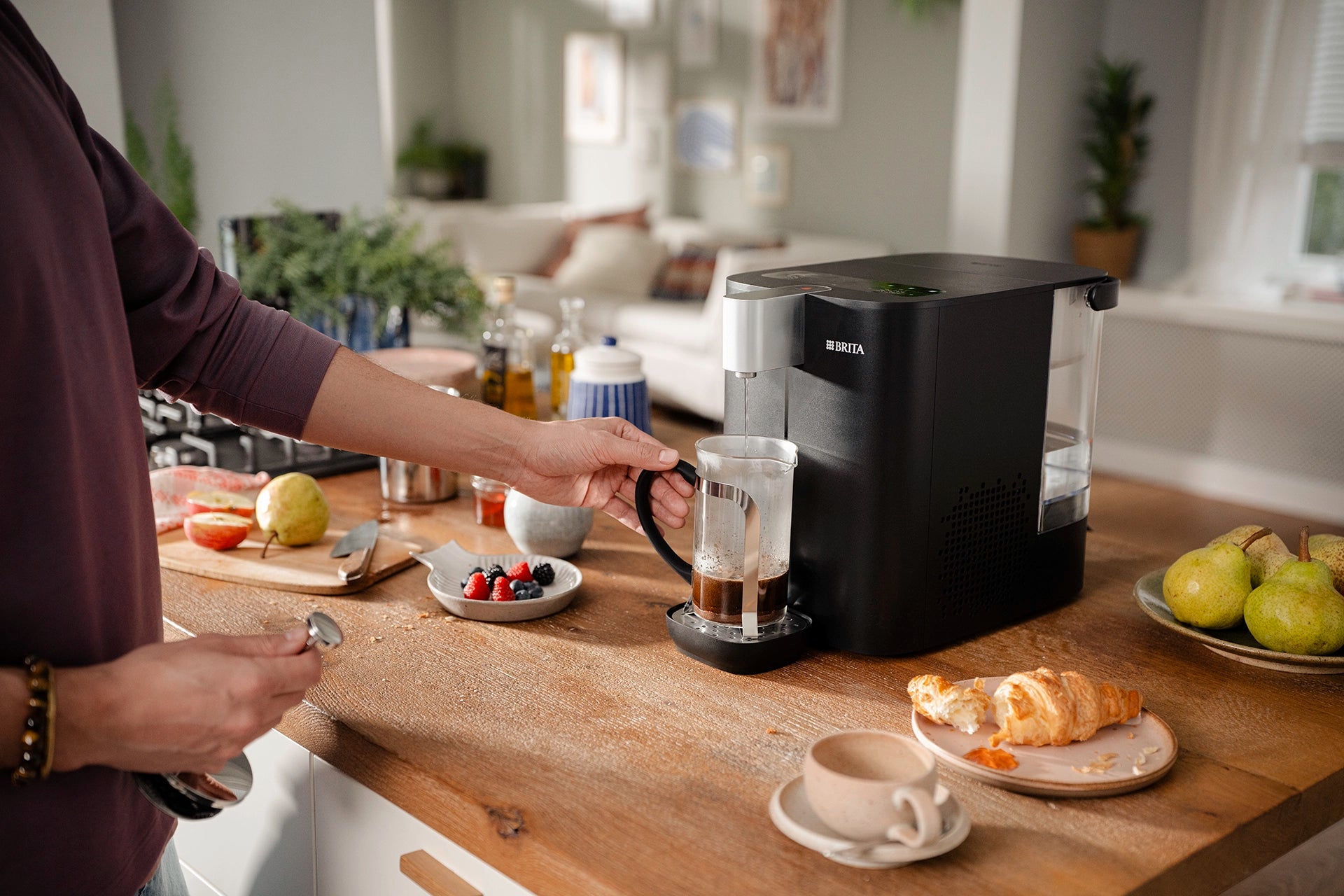 Person making coffee using YOURCE cool water dispenser on a wooden kitchen counter.