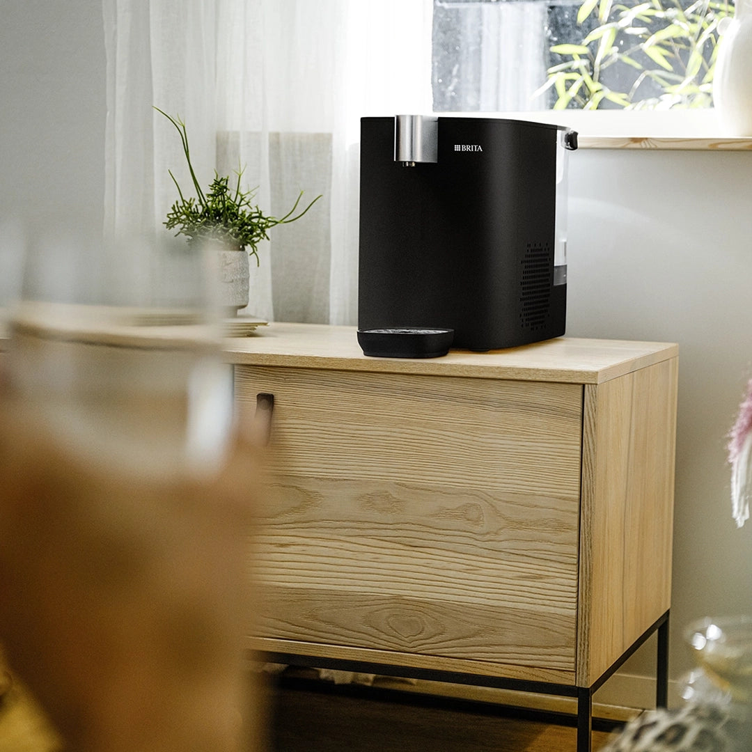 Black BRITA YOURCE cool water dispenser displayed on a wooden cabinet in a living room setting