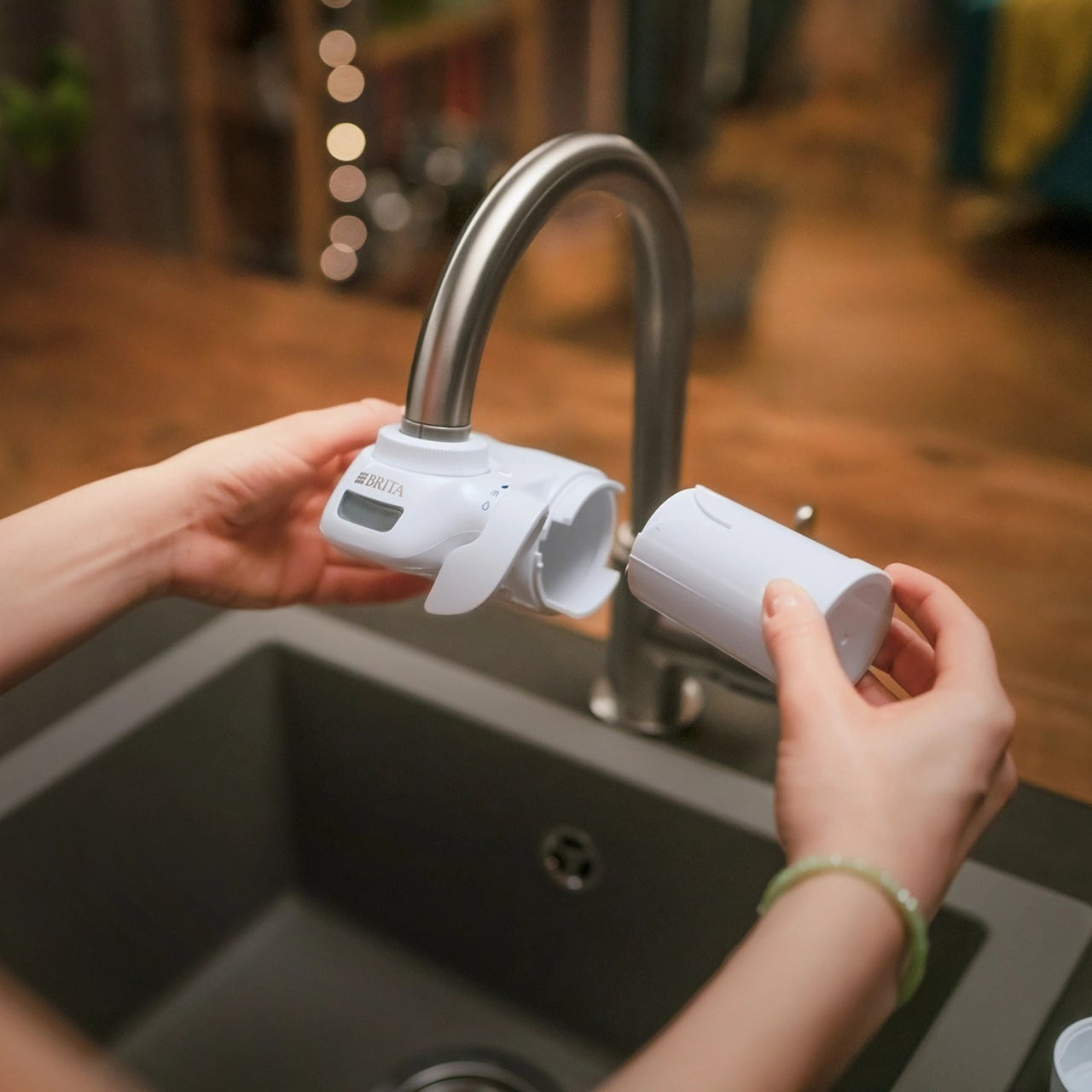Person replacing the filter cartridge on a BRITA ON TAP Pro water filter at a kitchen tap.
